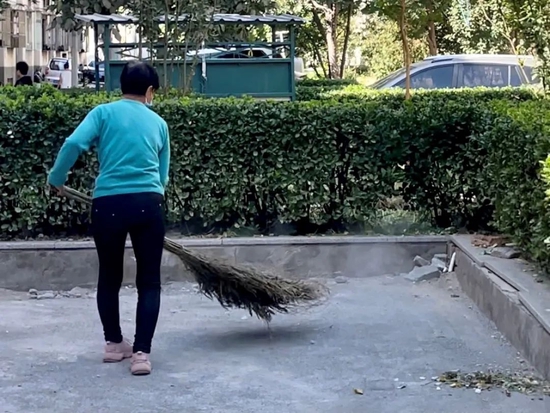 何明英在扫地,扫帚扬起一片尘土。摄影/郑可书